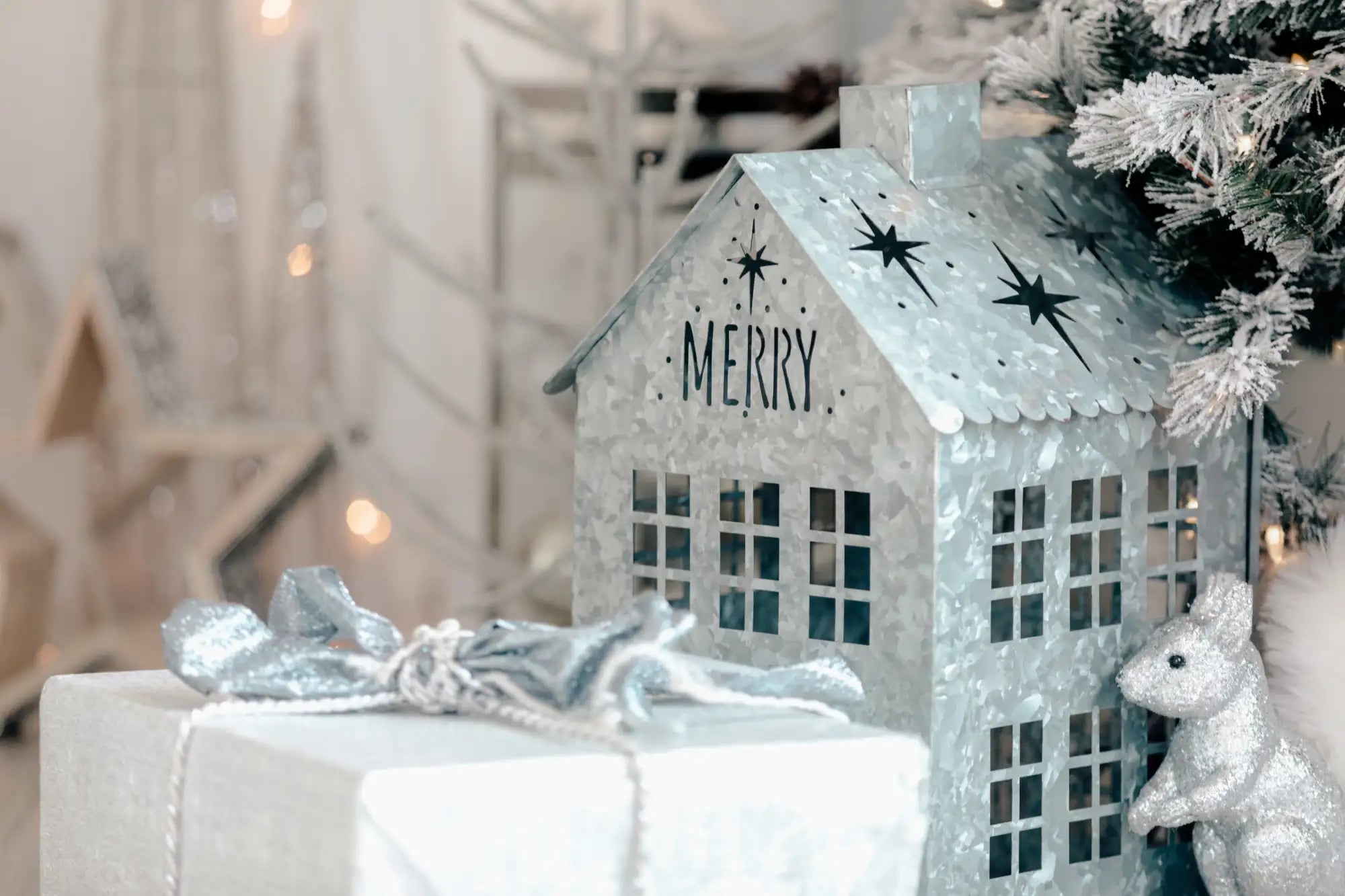 Silver metallic house-shaped lantern with black star cutouts and ’merry’ lettering on the front.