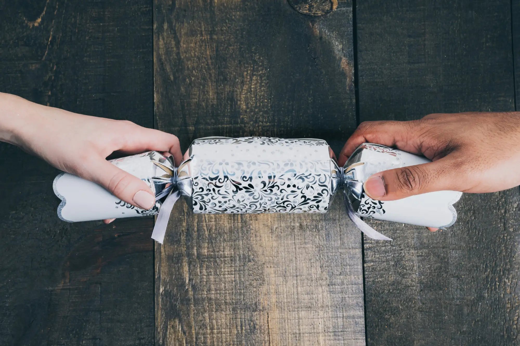 A white and black ornate paper christmas cracker with silver foil ends.
