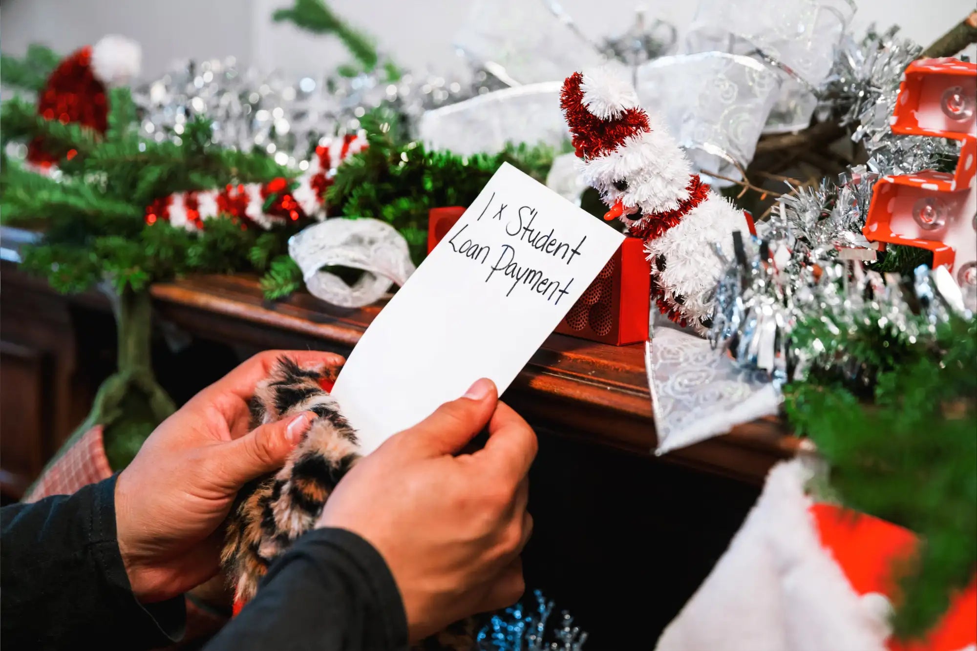 A white paper note with black handwritten text reading ’1 x student loan payment’ held in hands.