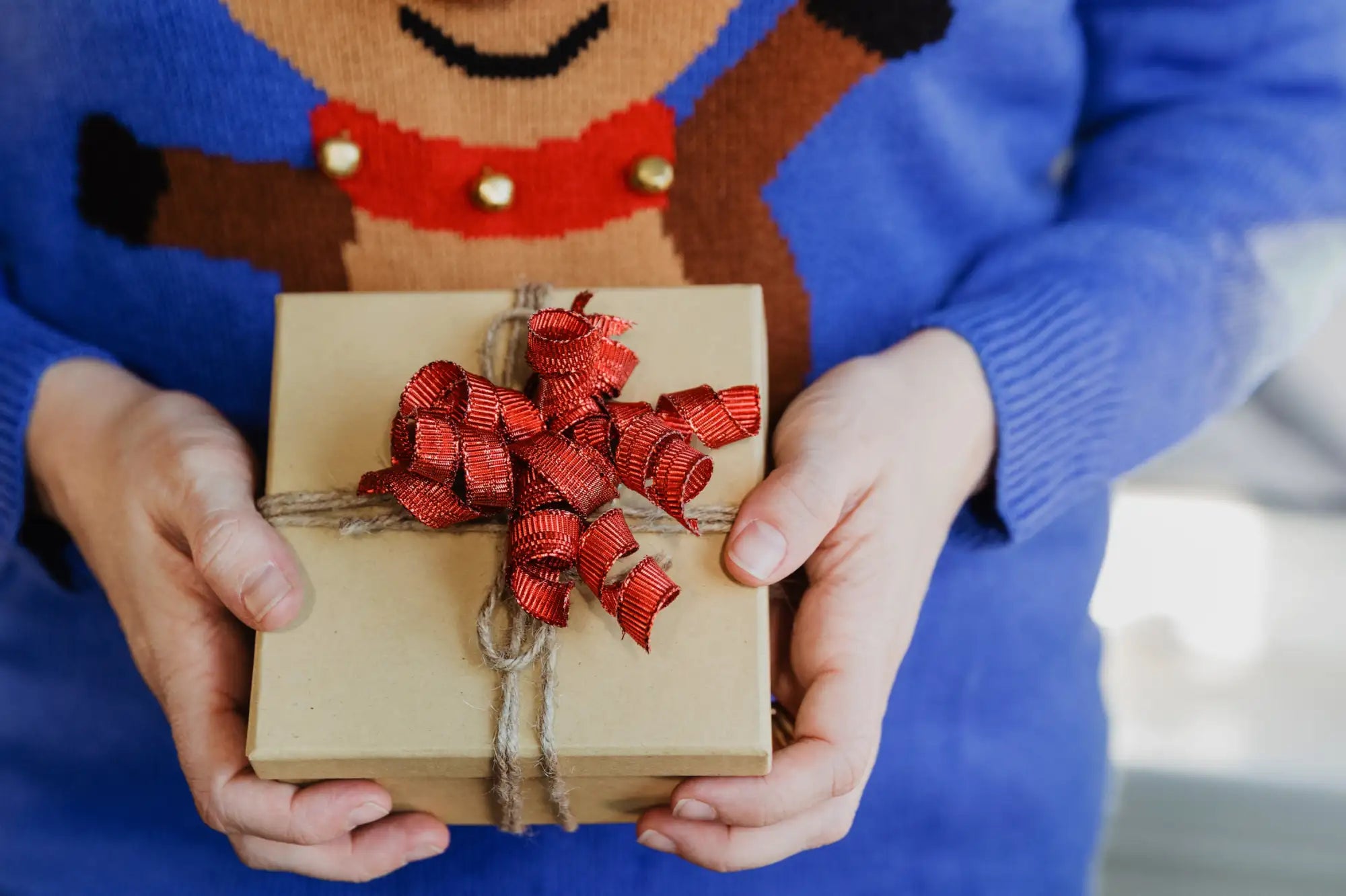 A beige gift box adorned with a vibrant red ribbon bow and tied with natural twine.