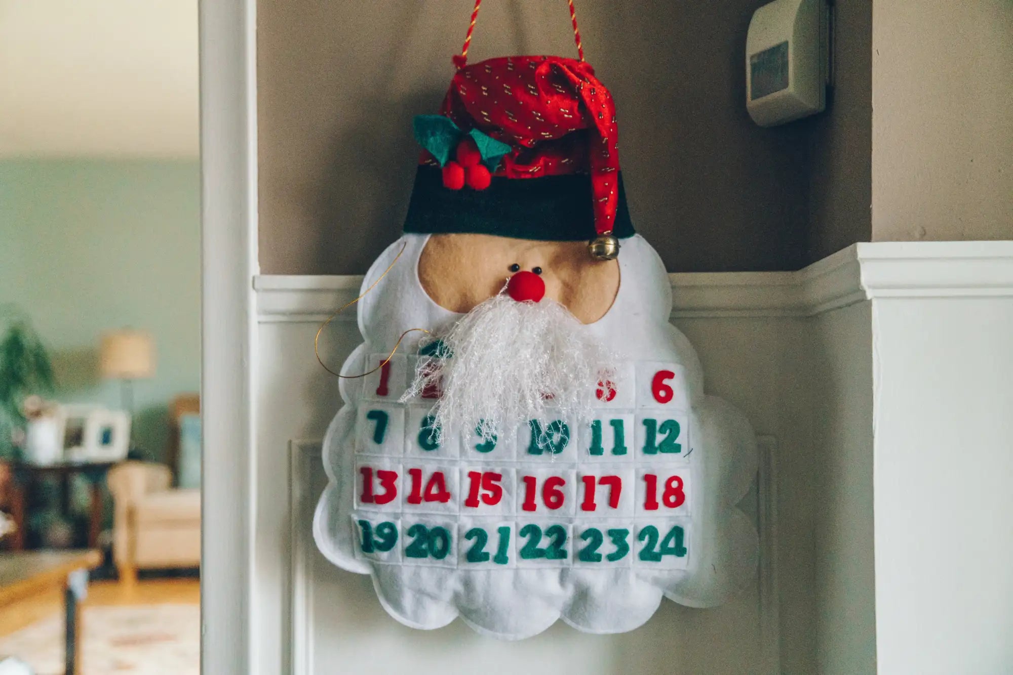 White felt santa claus-shaped advent calendar with red and green numbered pockets, a red hat adorned with holly berries, and a fluffy white beard.